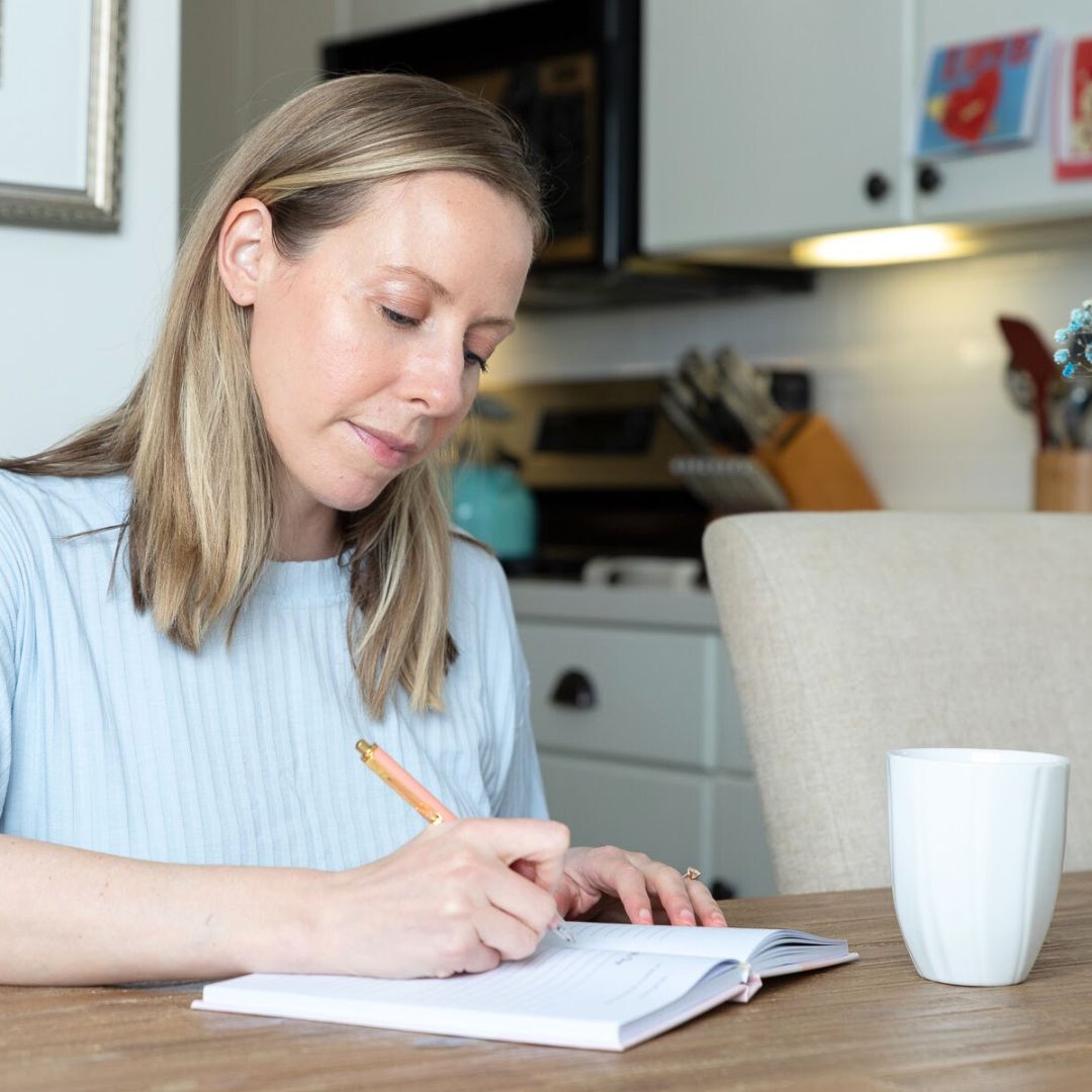Woman writing in daily reflection journal with coffee