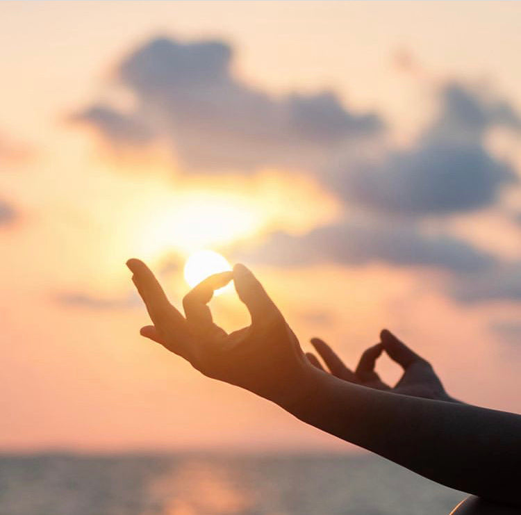 hands in meditation against sunset