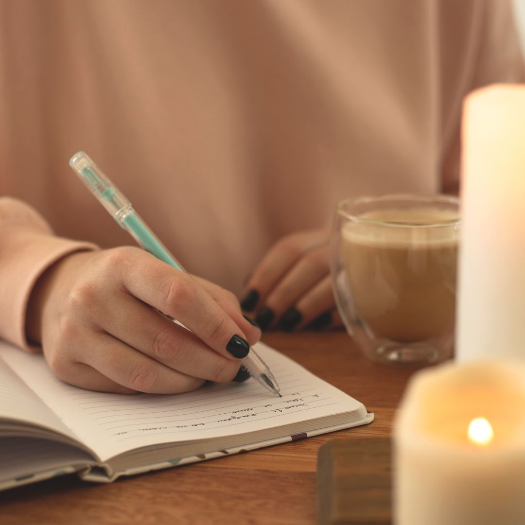 Woman journaling in blank notebook with lit candle